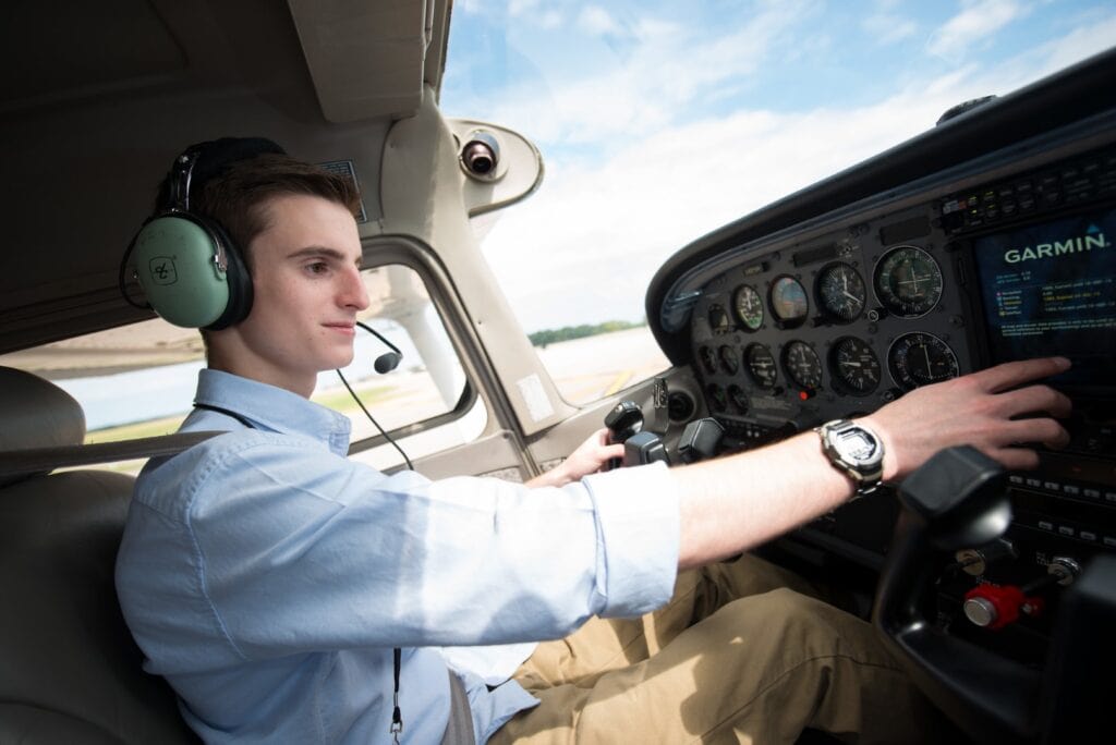 A young man sits in the cockpit of an airplane as part of his education in the professional pilot technology program.