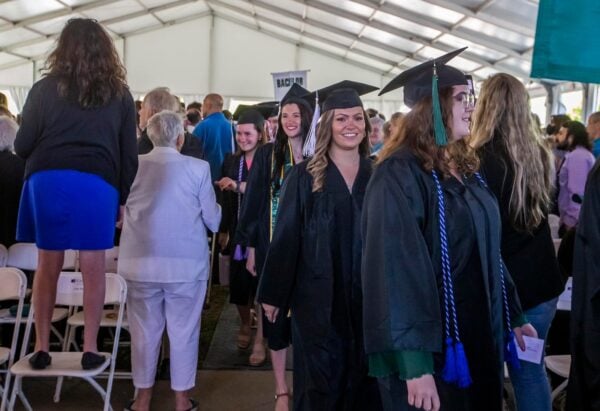 A line of Castleton graduates walk through a crowd of cheering families and friends.