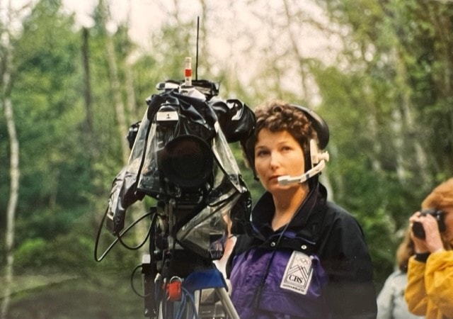 A woman with a headset microphone holder a giant video camera on her shoulder.