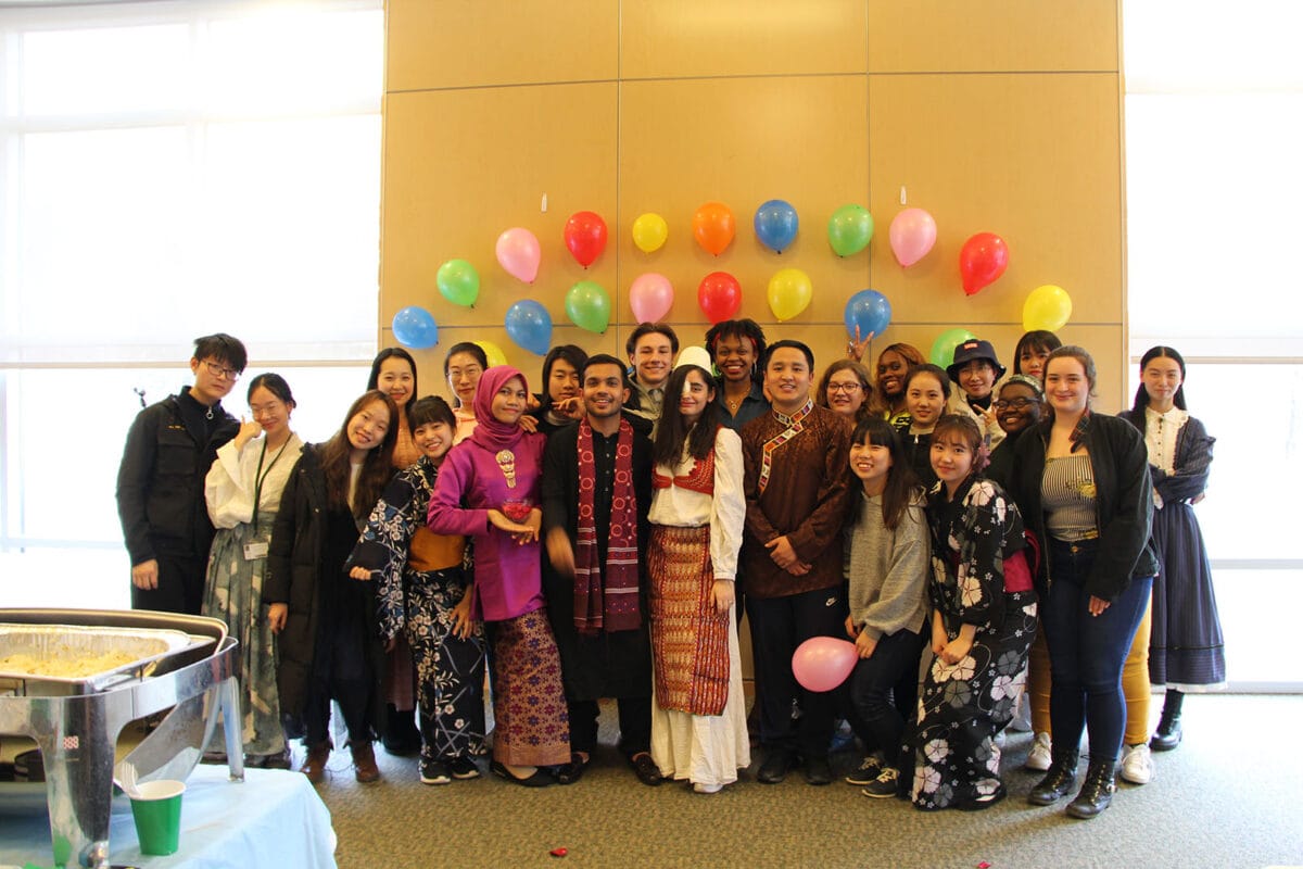 A large group of diverse students gather for a photo with balloons in the background.
