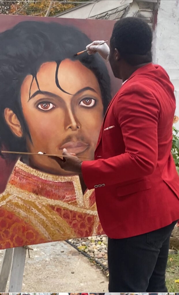Dodji Koudakpo in a red suite coat painting Michael Jackson. 