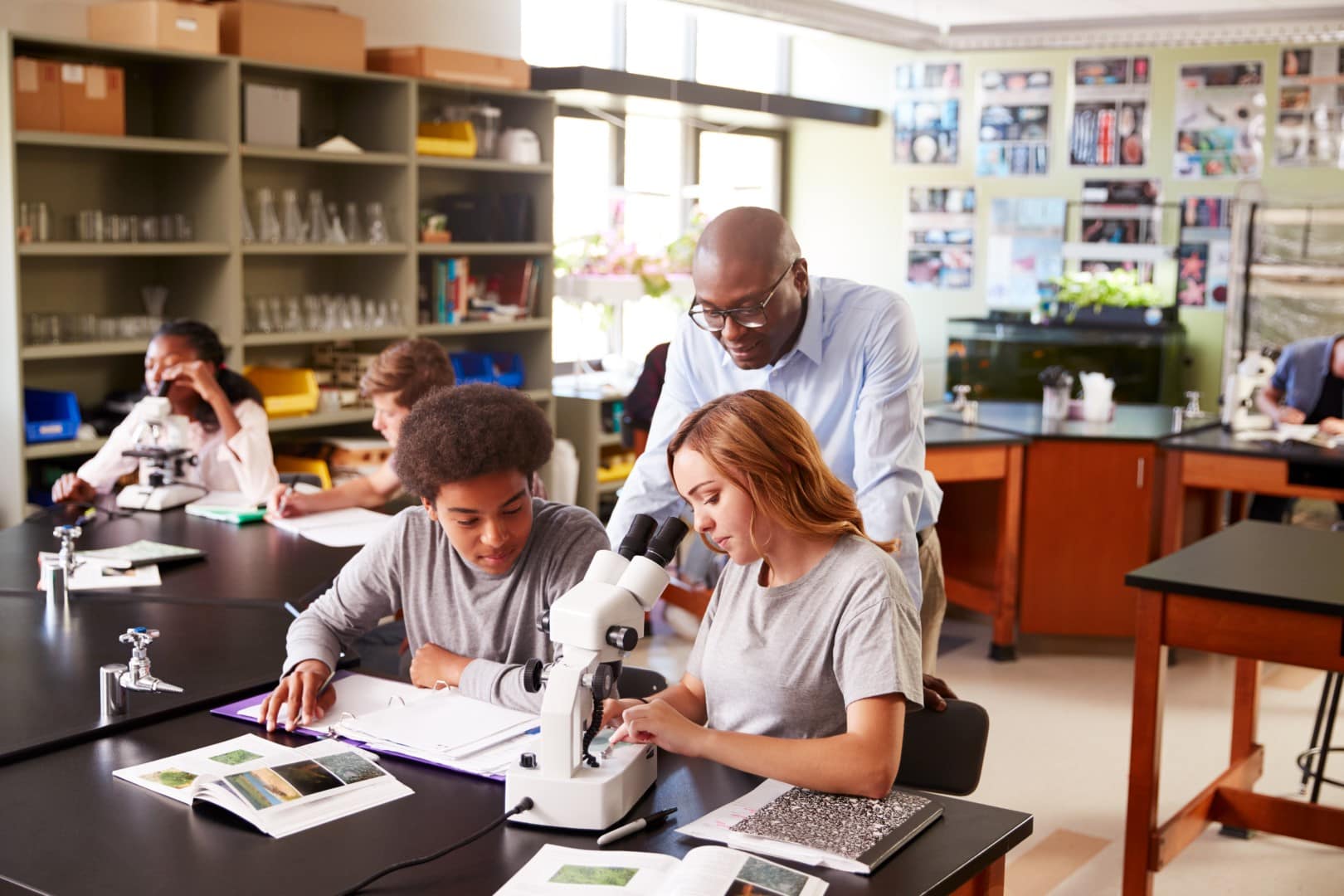 High school students with teacher using microscope in science class.