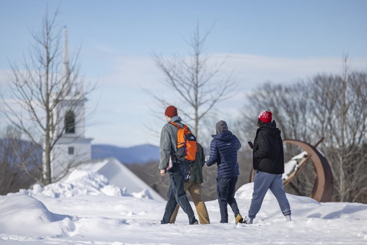 A group of three students walking in the snow on a Vermont State University campus.