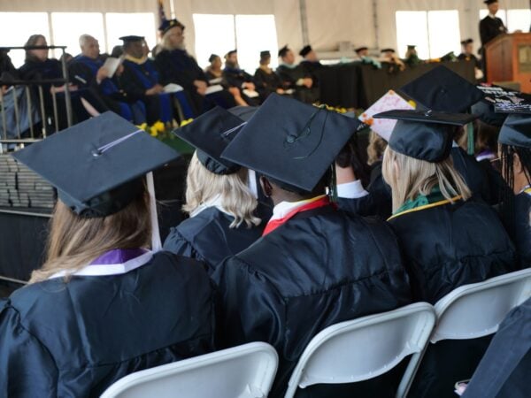 A group of Vermont State University graduating seniors from behind as they sit wearing graduation caps.