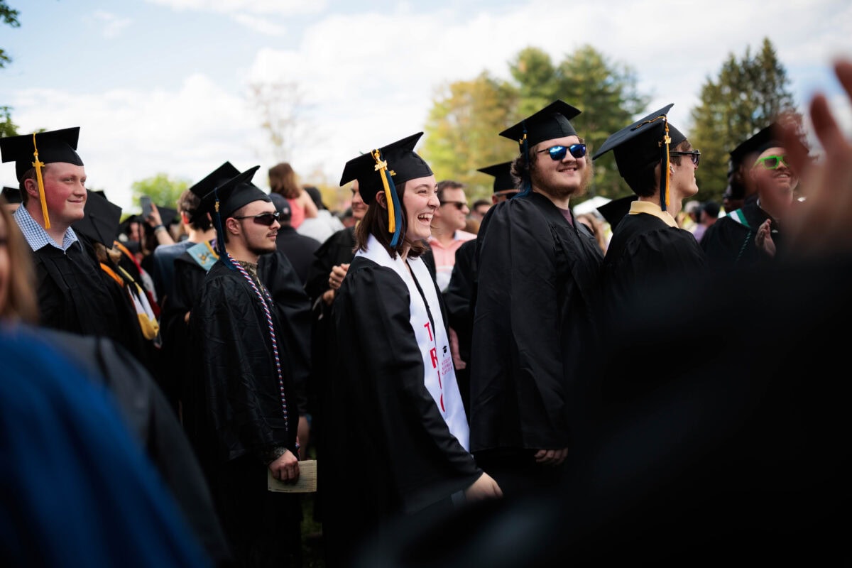 A group of students wearing caps and gowns walking outside as they enter their commencement ceremony