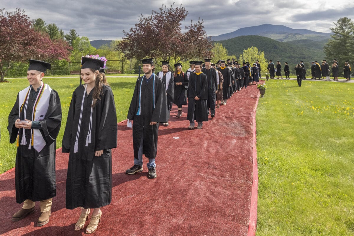 Graduates wearing caps and gowns walking in a line to enter their commencement ceremony.