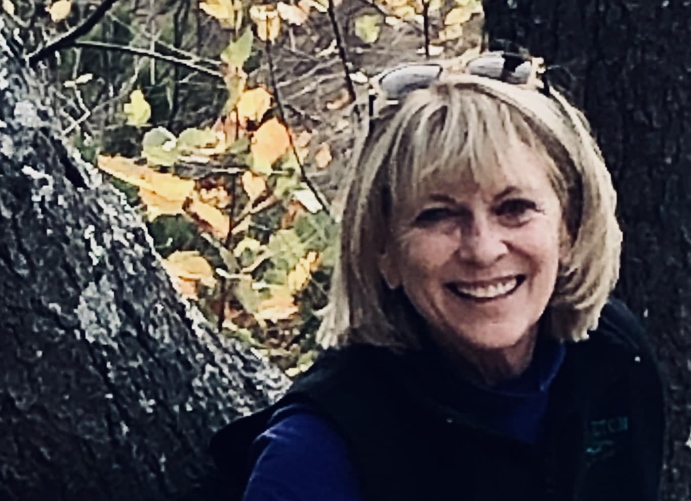 Martha Coulter smiles at the camera with trees and foliage in the background.