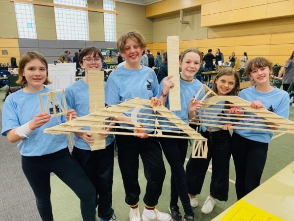 The winning team of the Vermont State Bridge Building Competition all dressed in blue holding the remnants of their popsicle stick bridge.