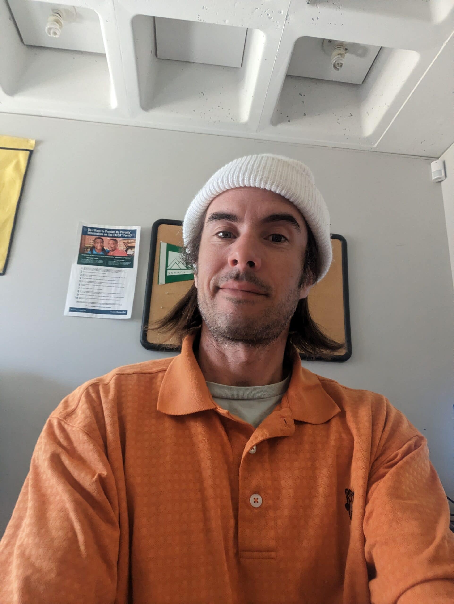 Andrew D'Aversa Smiles at the camera in a orange button up and white beanie.