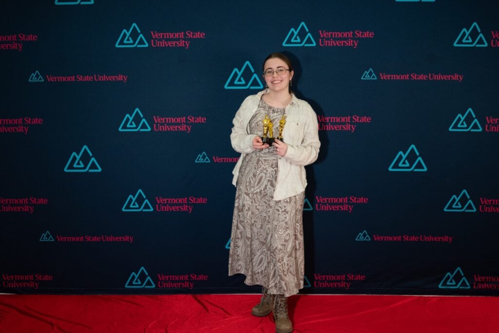 A young woman in a dress stands on a red carpet at Vermont State University Lyndon.