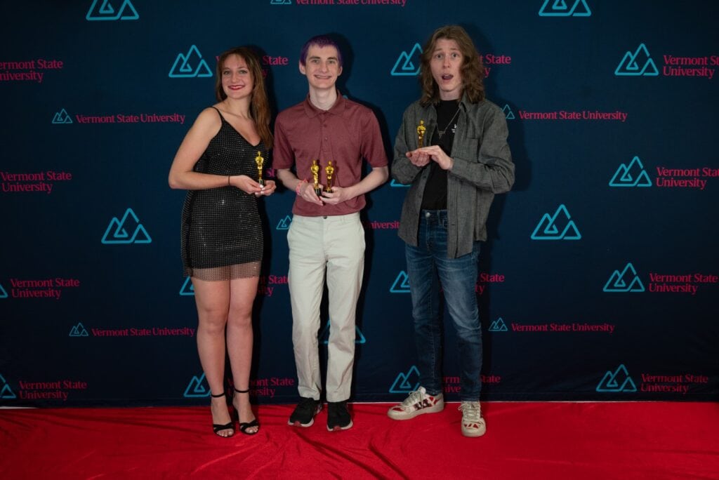 Three Vermont State University Students stand together on a red carpet.
