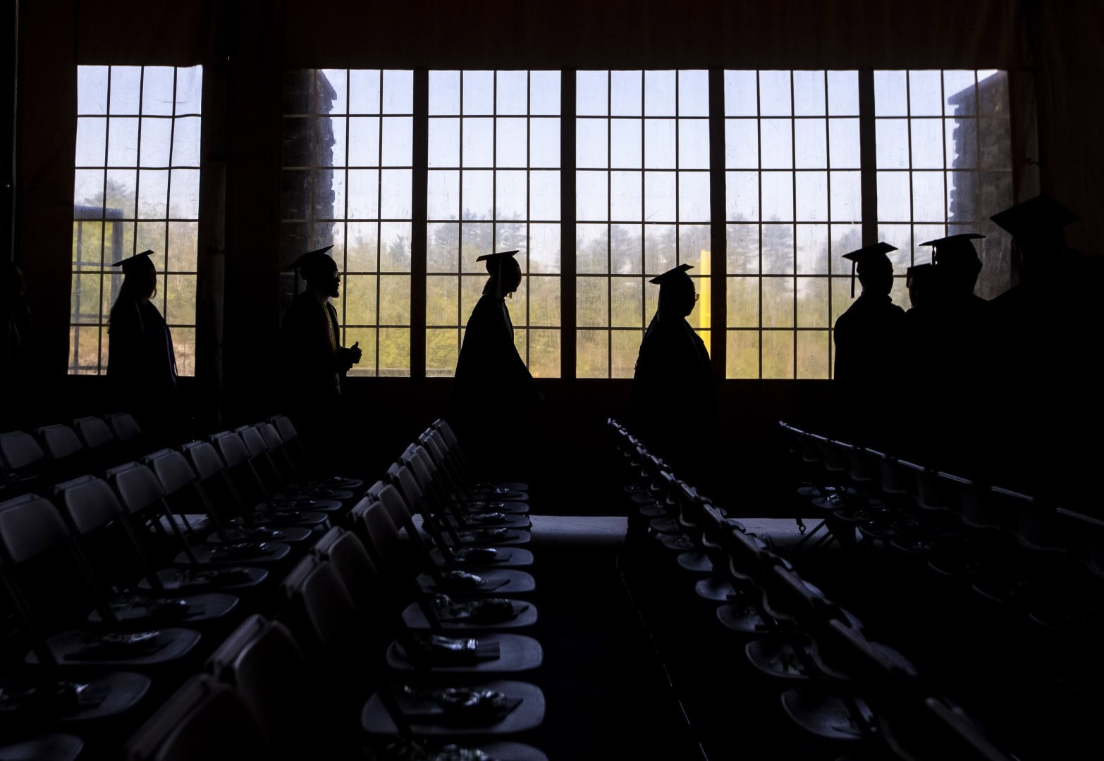 A line of Vermont State University graduates silhouetted against a window.