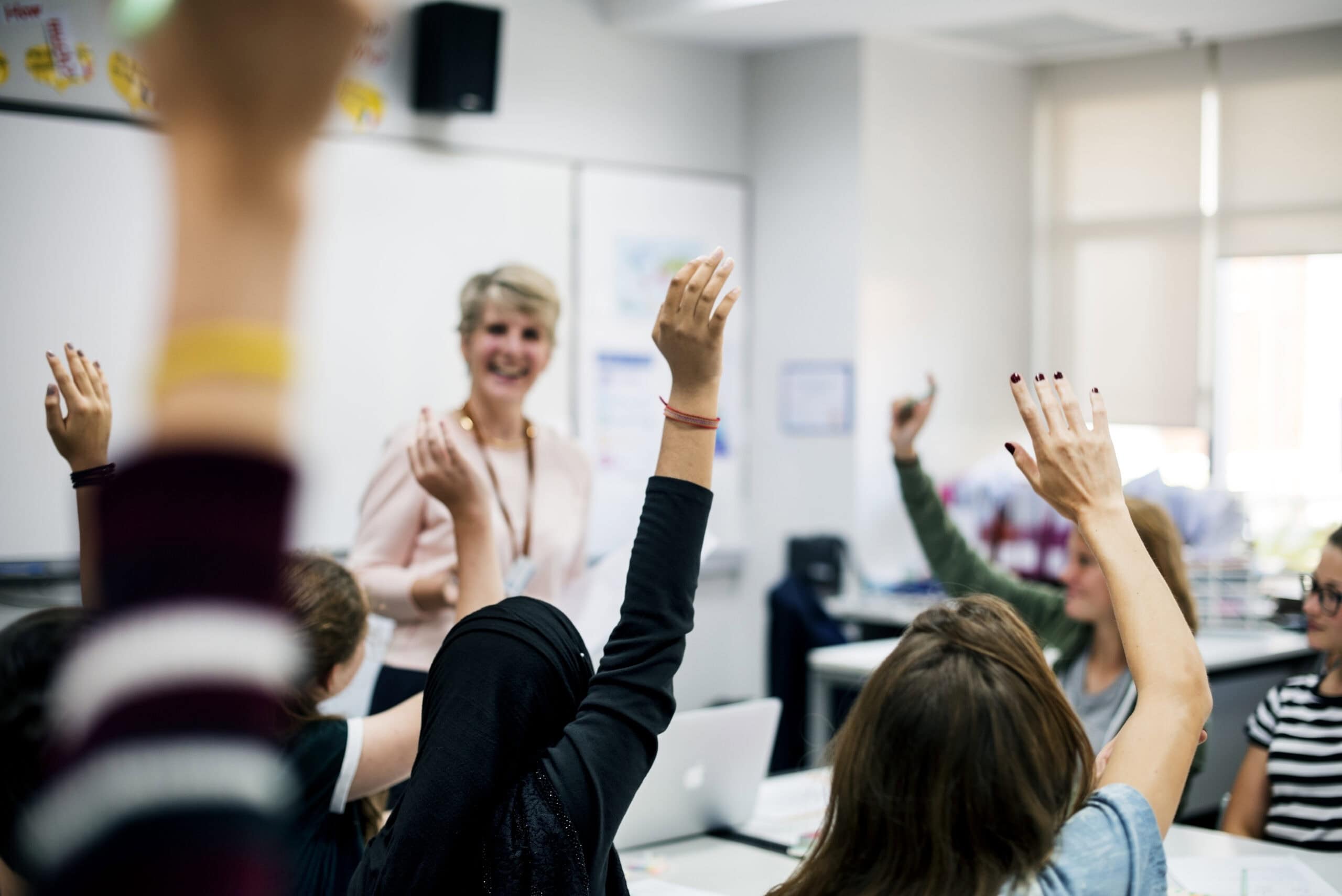 Group of students raising their hands in a classroom.
