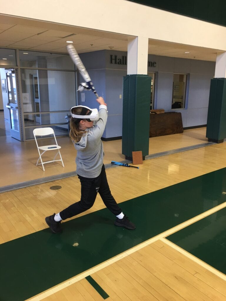 A person wearing a grey hoodie and a VR head set to simulate batting practice. 