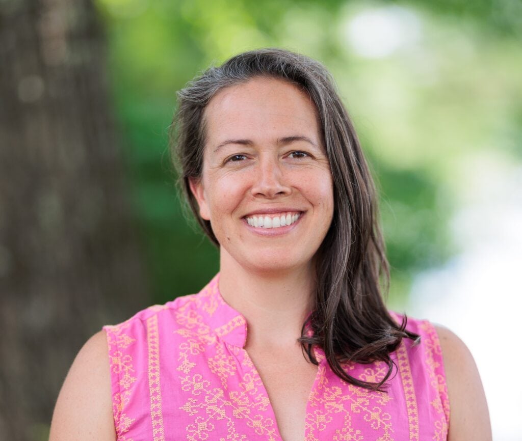 Hannah Reid, a woman with shoulder length brown hair wearing a pink shirt, smiling at the camera.