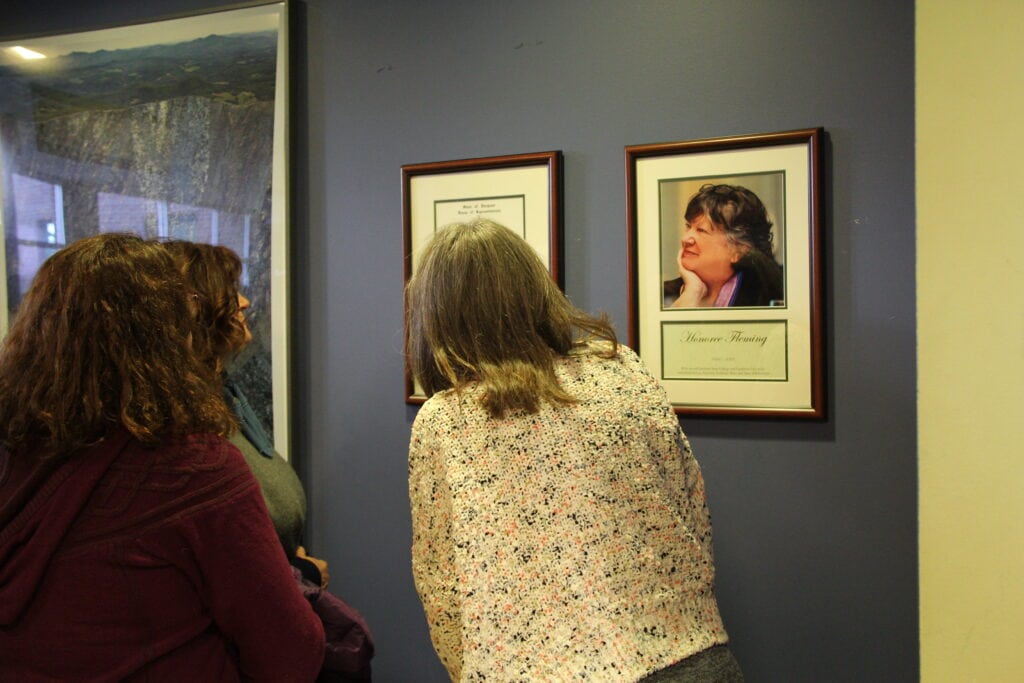 Community members looking at framed photo of Honoree Fleming memorial hanging on the wall. 