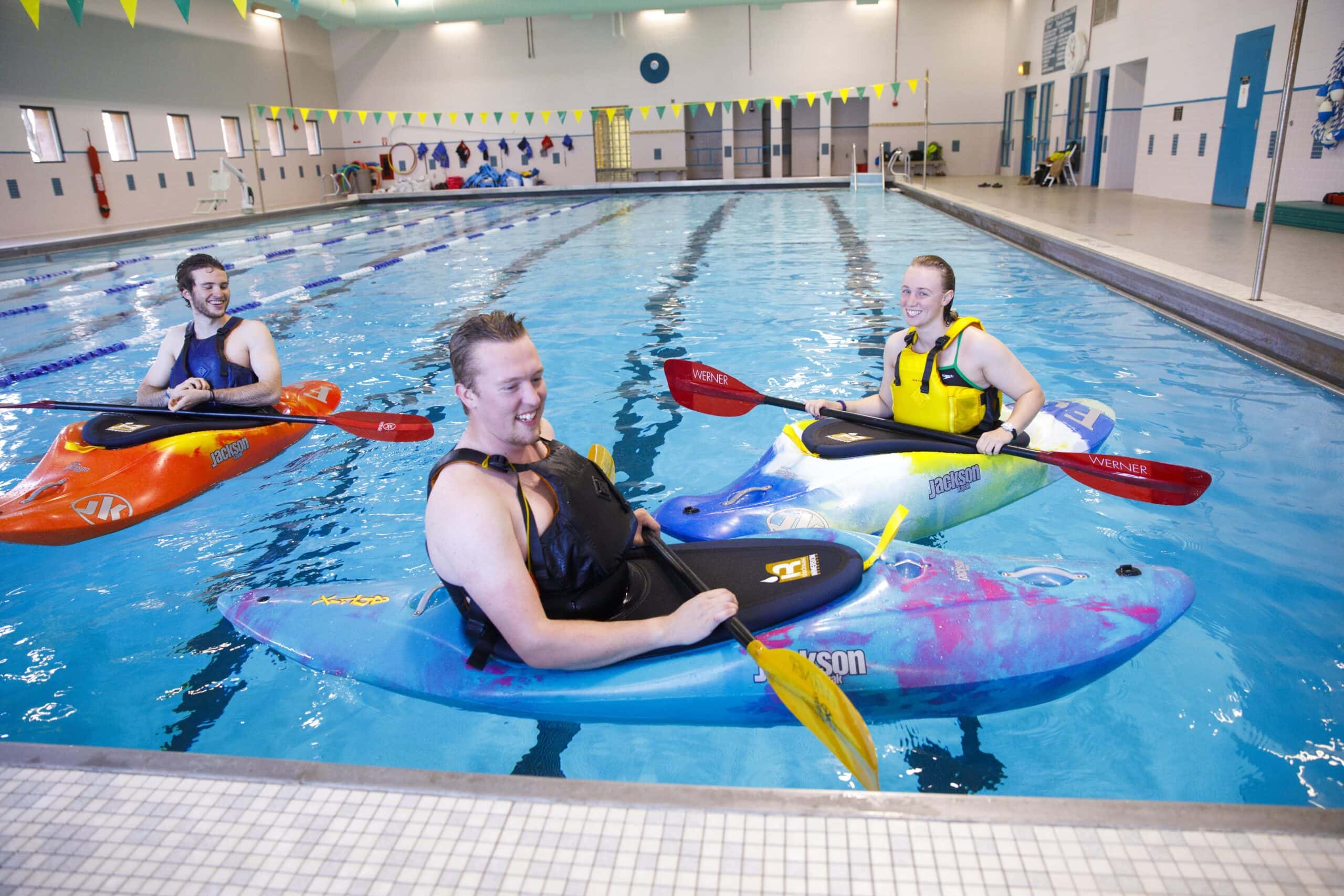 Three kayakers in an indoor pool at the Vermont State Lyndon campus.