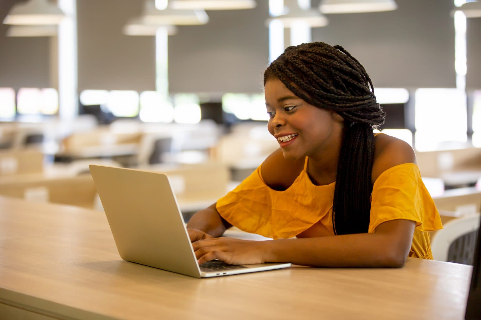 A woman sits at a table with her laptop smiling.