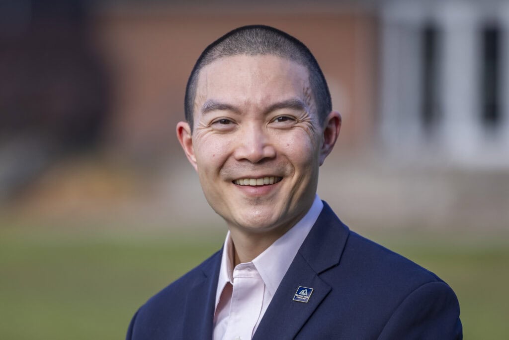 A man with short black hair wearing a blue suit smiling at the camera.