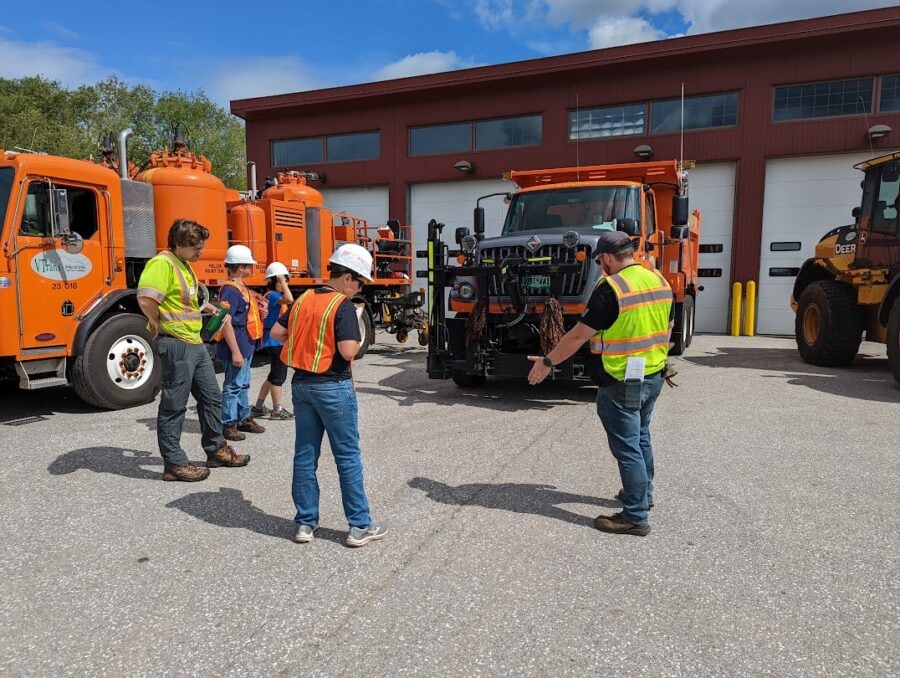 Volunteers from the transportation agency in high visibility vests are educating students about a truck in a parking lot