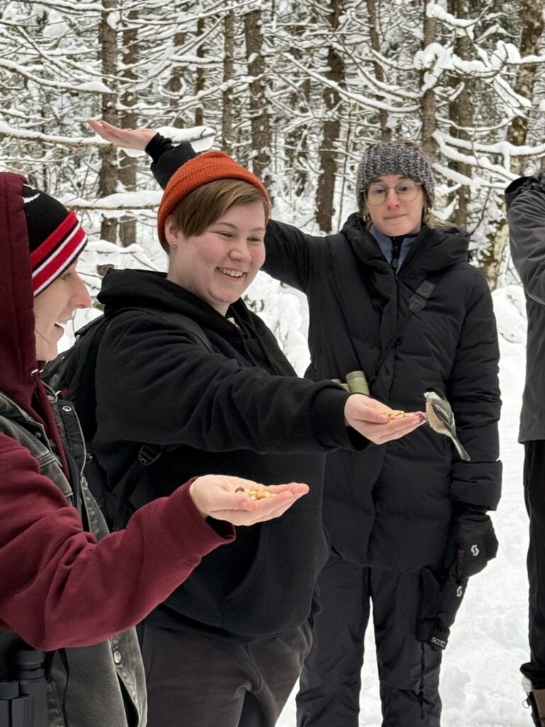 Students in a snowy forest hold their hands out and a bird lands on one.