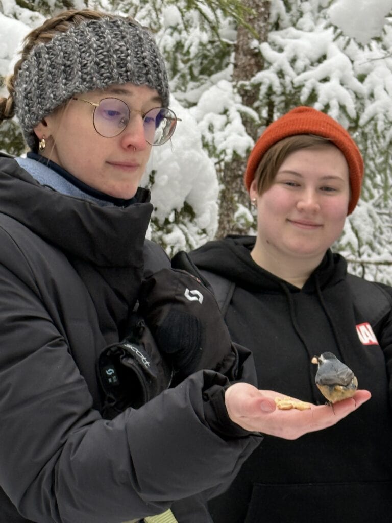 Students in a snowy forest hold their hands out and a bird lands on one.