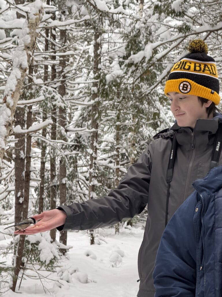 Students in a snowy forest hold their hands out and a bird lands on one.