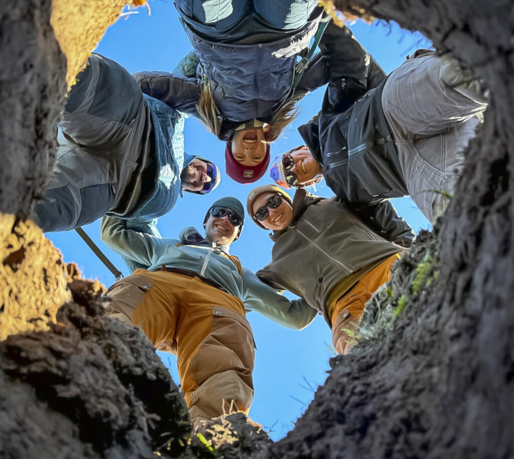 A group of people latch arms and look into a hole.