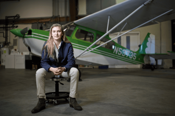 Female pilot student sits in front of Cessna aircraft in hanger at Burlington airport.