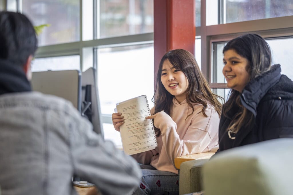 Three international students sitting together at a table discussing notes.