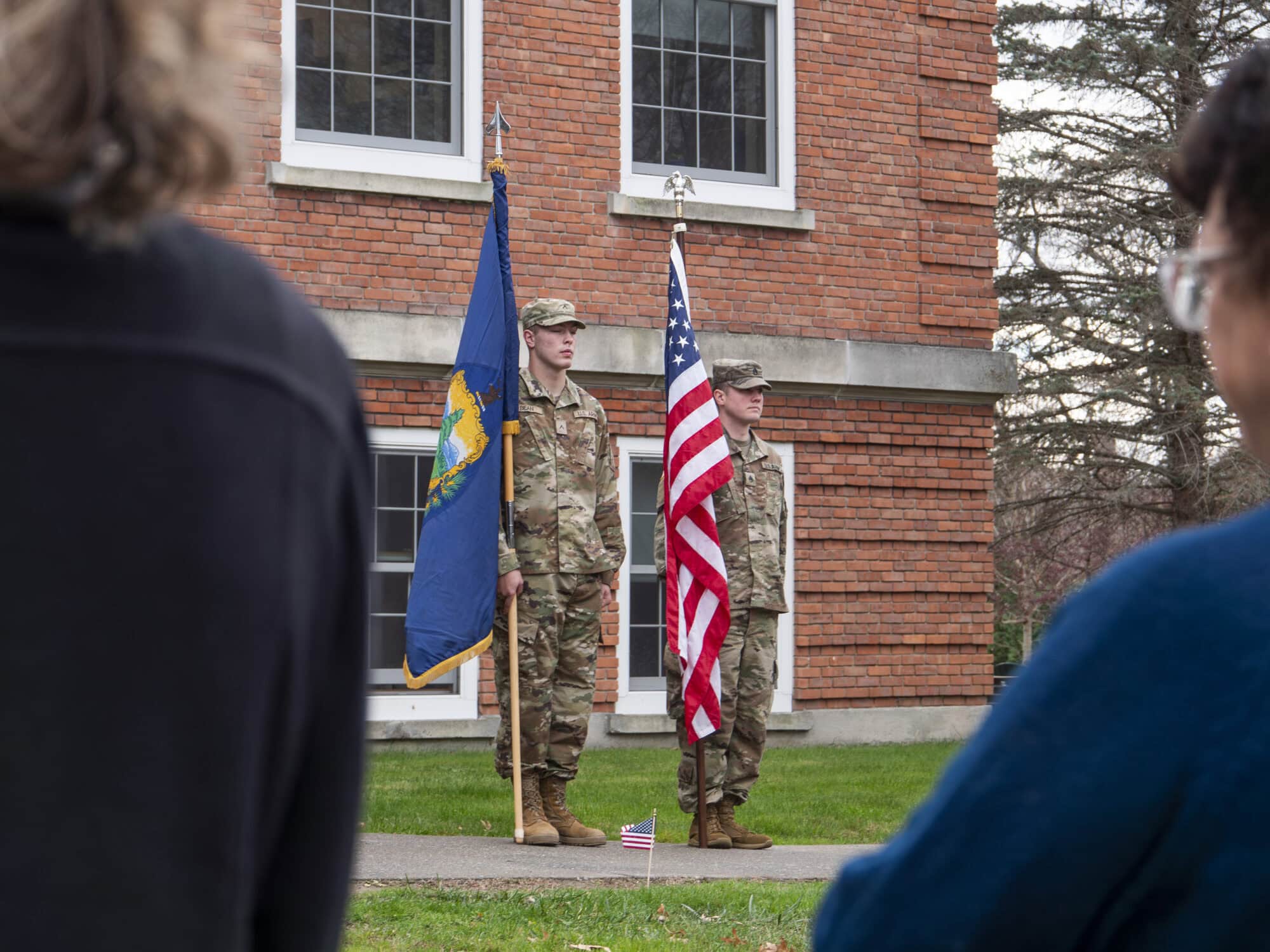 Two men in military uniforms standing side by side. One holds the state of Vermont flag, and the other holds the United States flag.