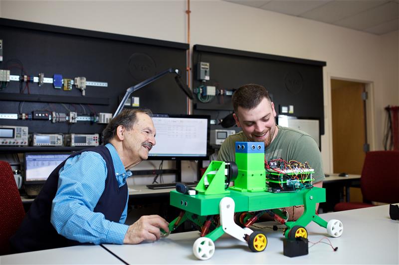 Two men lean over a robot on the Vermont State University Randolph campus.