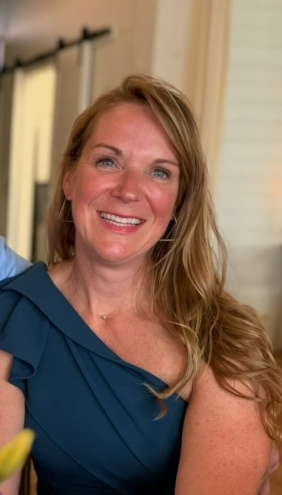 Mary Hill smiling at the camera while wearing a dark blue dress