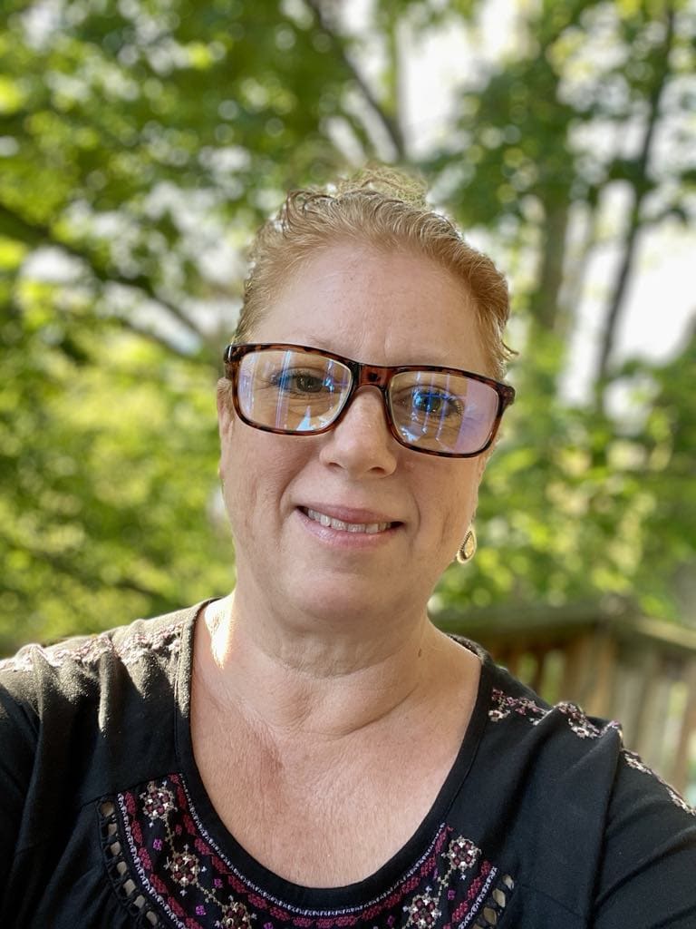 Pam Alexander smiling at the camera while wearing a dark shirt and rectangular glasses.