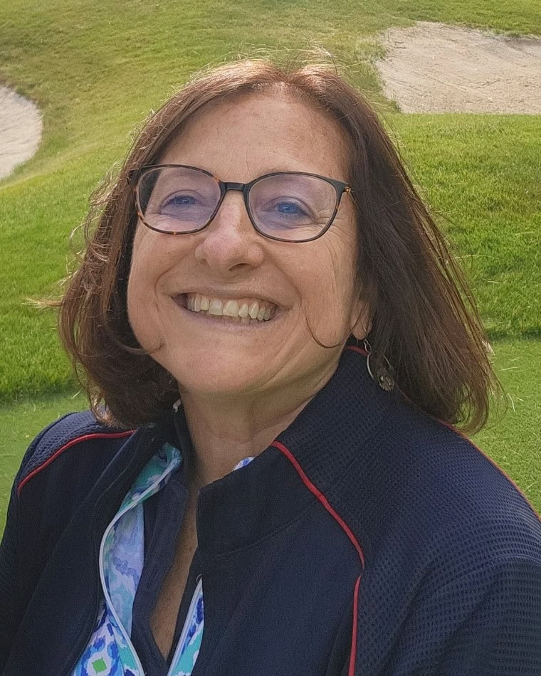 Susan Shayne smiling at the camera while standing outside wearing black glasses and a blue jacket