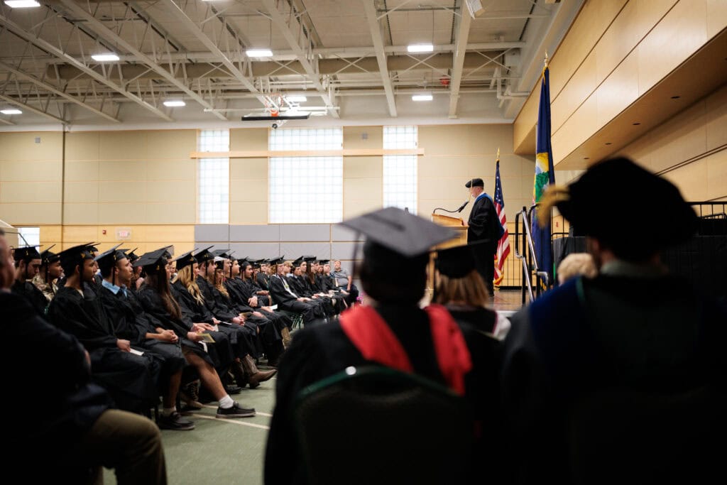 A large group of graduates seated looking toward a speaker at a podium
