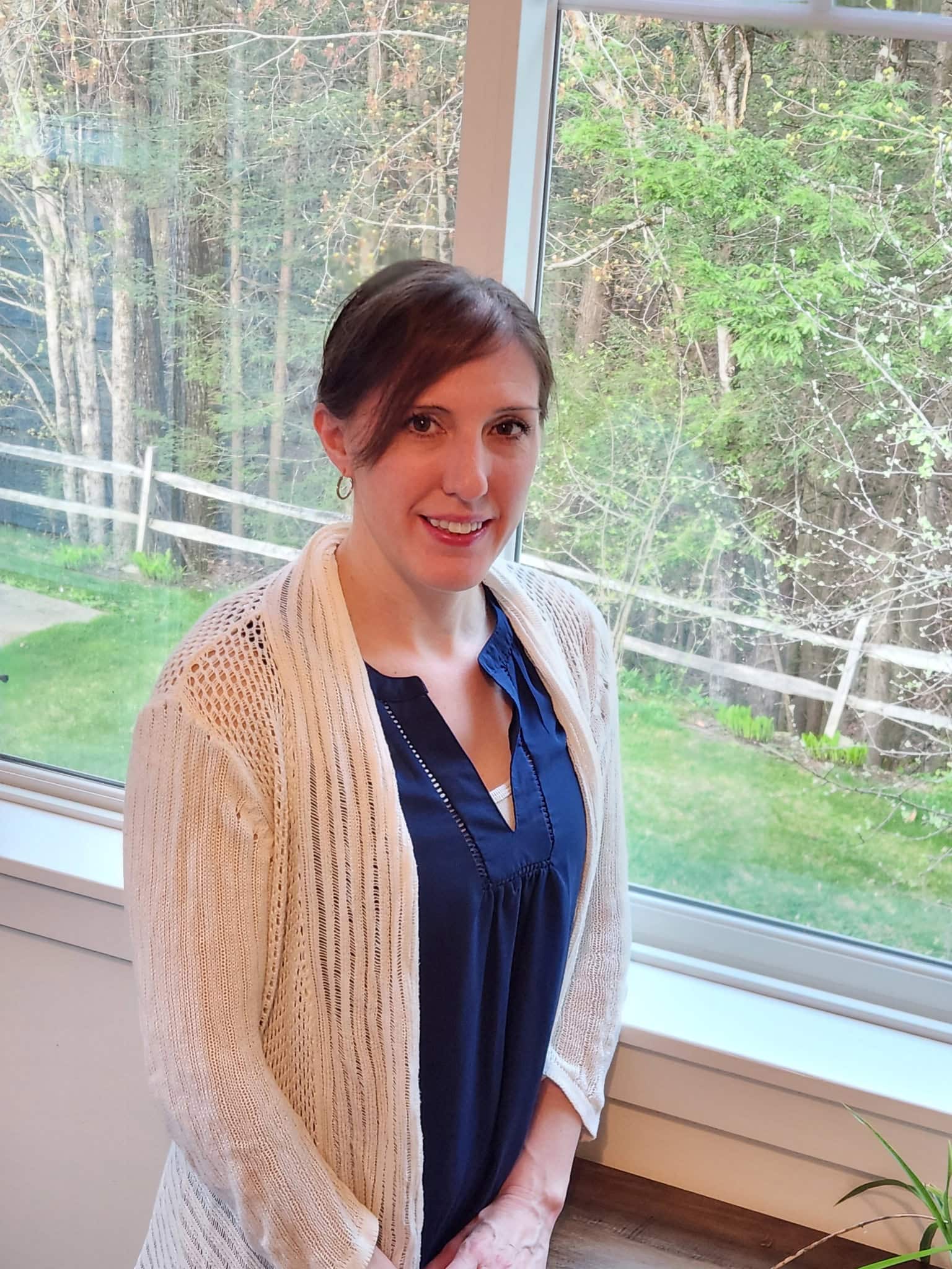 Bethany Crowley smiling at the camera while wearing a blue shirt with a white cardigan sweater layered on top.