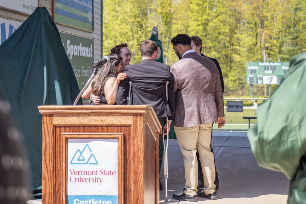 Students standing in group talking behind podium with arms around each other