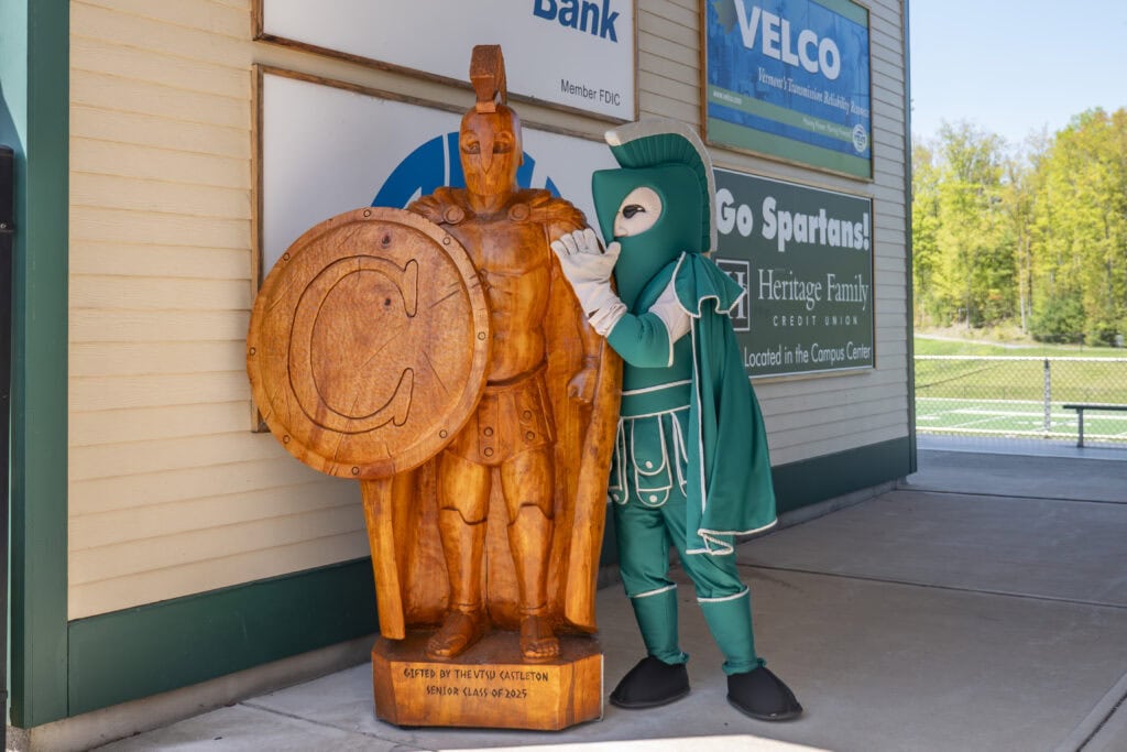 Spartan mascot stands alongside wooden carved Sparty statue