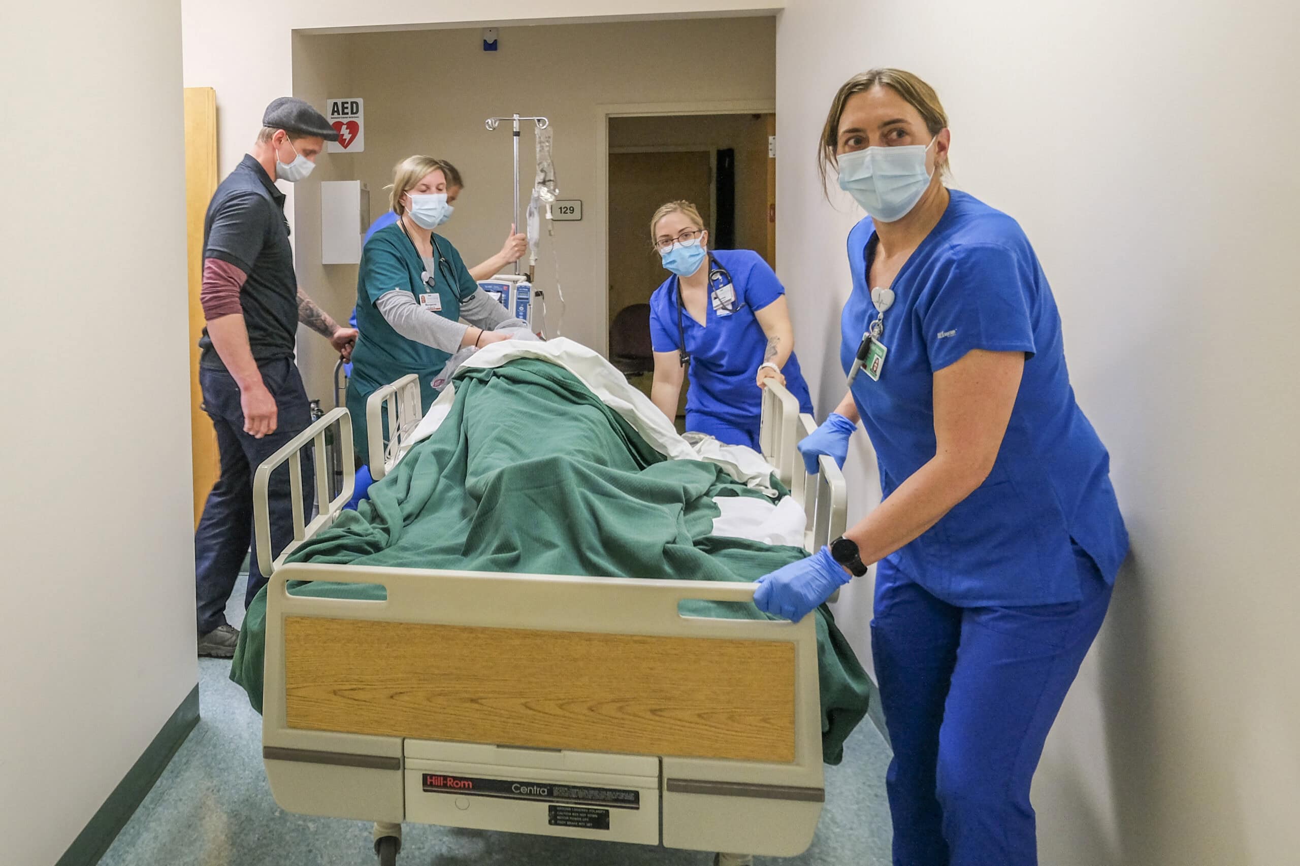 Nursing students wheel a patient on a bed through a hallway