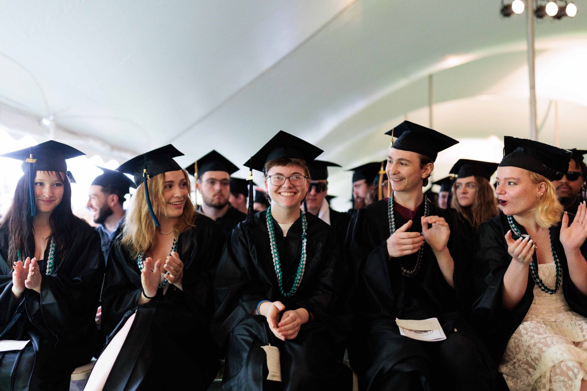 A group of graduates in black caps and gowns smiling at the camera at the VTSU Randolph 2025 Commencement ceremony