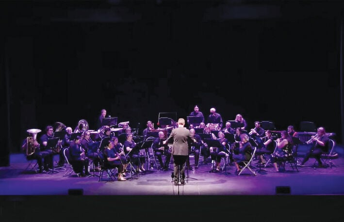 The Johnson Concert Band set up on the Dibden stage performing a concert. The group is illuminated with a deep purple light.