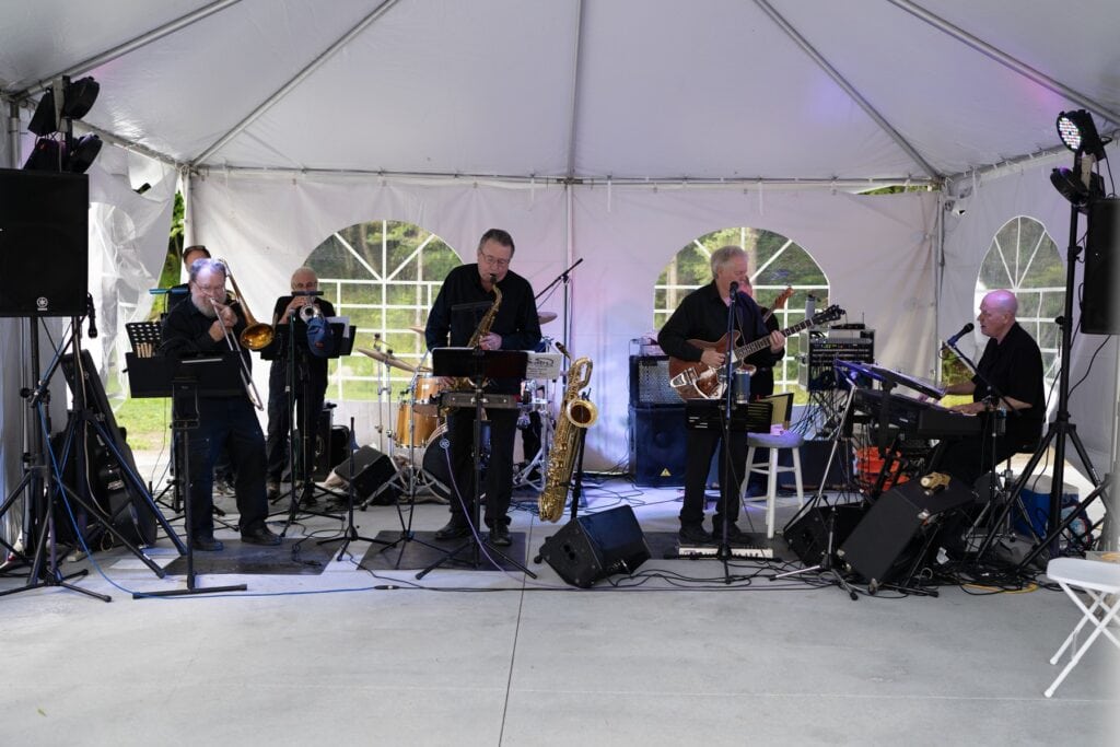 Members of Stain and Steel all dressed in black performing under a white event tent.
