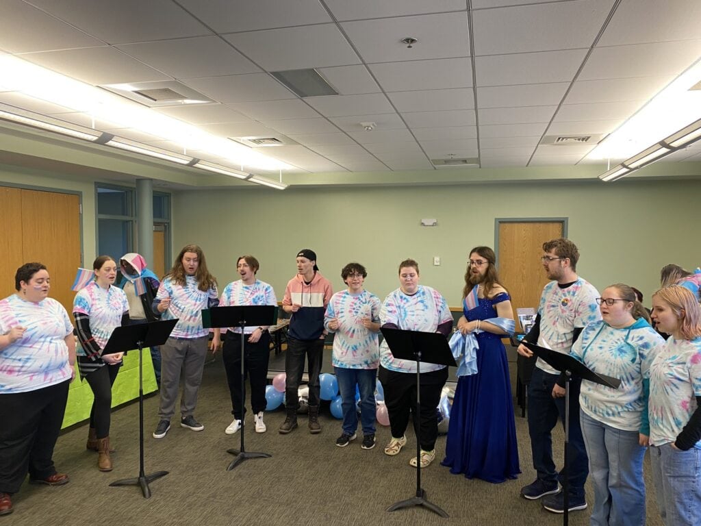 Vocal Unrest members standing in a semi-circle while performing. They're wearing blue and pink tie-die shirts, and one member is wearing a blue dress. 