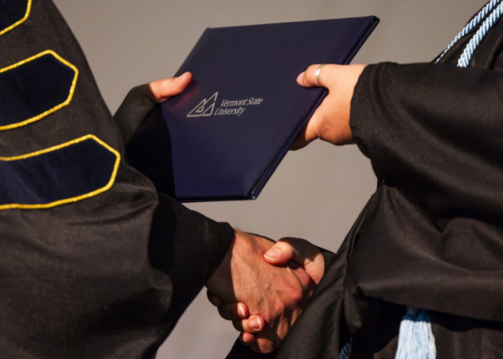 A closeup photo of a hands exchanging a diploma at VTSU graduation