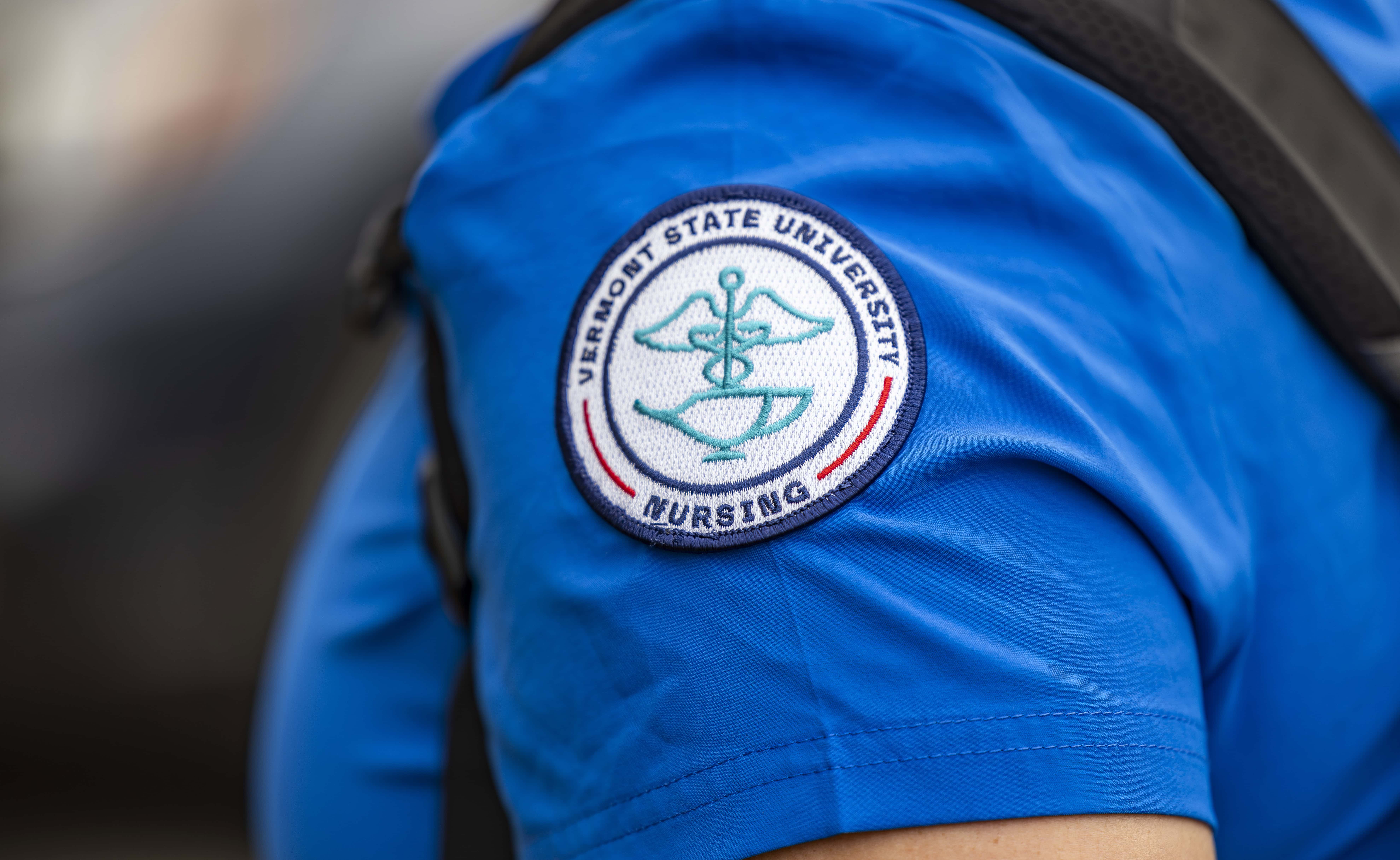 An embroidered VTSU Nursing seal patch on the shoulder of a blue set of scrubs.