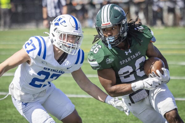 A VTSU Castleton football player running with the ball as an opponent tries to intercept.