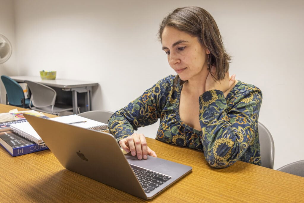 A woman with shoulder length brown hair working at a laptop