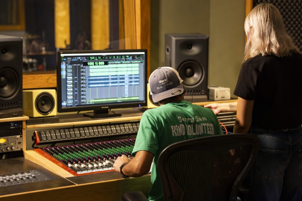 A student with their back to the camera sitting at an audio mixing board in the VTSU Lyndon recording studio