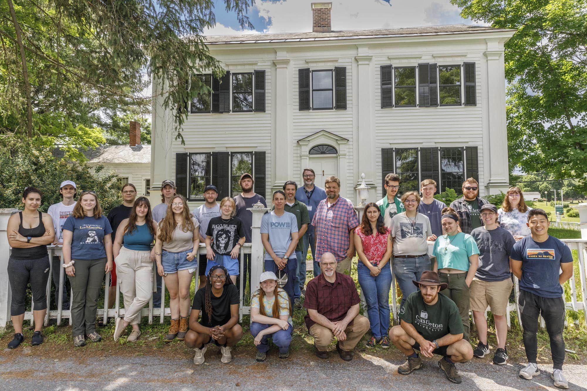 A group of students and faculty members stand in front of a historic white home.